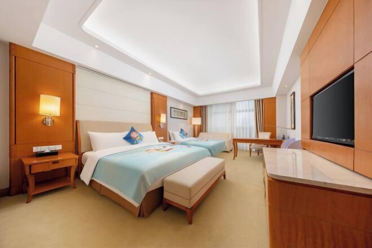 Habitación de hotel con dos camas, un escritorio, un televisor y una lámpara de techo.
