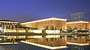 Un bâtiment moderne avec une fontaine dont l’eau reflète la lumière à l’avant, de grandes fenêtres et un ciel dégagé.