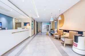 Un espace d’accueil d’hôtel comprenant un comptoir de réception, un coin salon et un téléviseur fixé au mur.