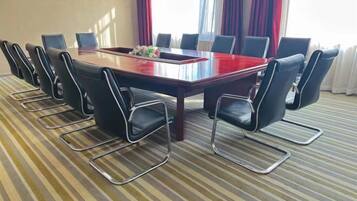 A conference room with a rectangular table surrounded by chairs, a carpeted floor, and curtains.
