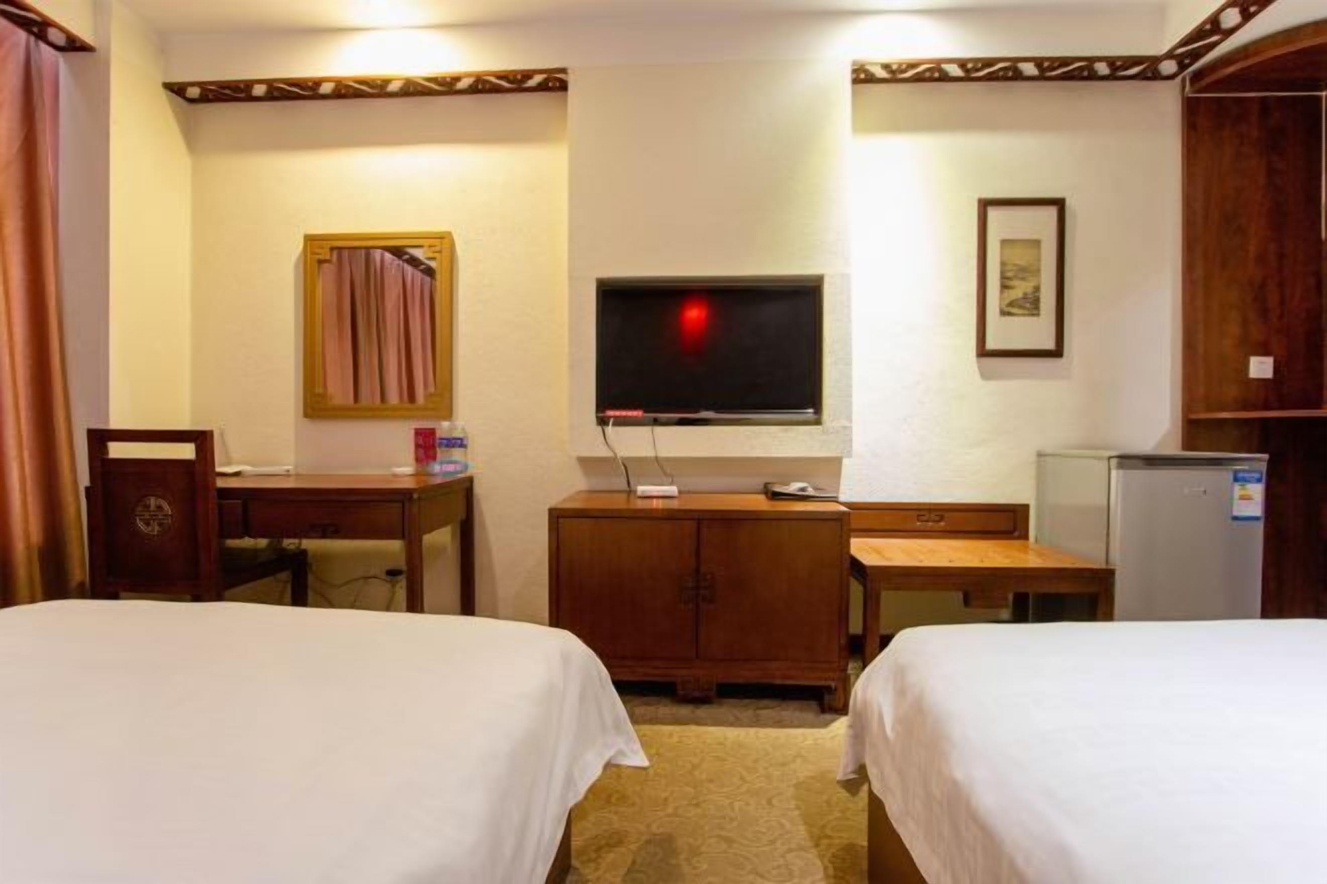 A hotel room with two beds, a TV, a desk, a cabinet, and a refrigerator.