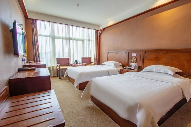 A hotel room with two beds, a desk, a chair, and a large window with curtains.