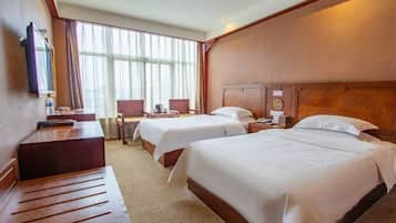 A hotel room with two beds, a desk, a chair, and a large window with curtains.