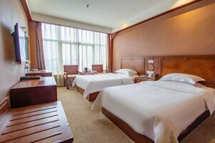 Habitación de hotel con dos camas, un escritorio, una silla y un ventanal con cortinas.