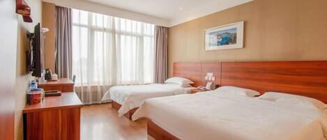 A hotel room with two beds, a wooden desk, a TV, and a window with curtains.