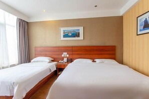 Habitación de hotel con dos camas, cabecero de madera, mesita de noche, un cuadro en la pared y una ventana con cortinas.