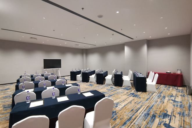 A conference room with a long table, chairs, a projector screen, and a red tablecloth.