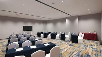 Una sala de conferencias con una mesa larga, sillas, una pantalla de proyector y un mantel rojo.