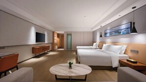 A modern hotel room with a large bed, a sofa, a TV, and a dining table.