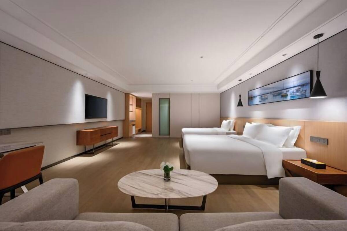 Ein modernes Hotelzimmer mit einem großen Bett, einer Couch, einem Fernseher und einem Esstisch.