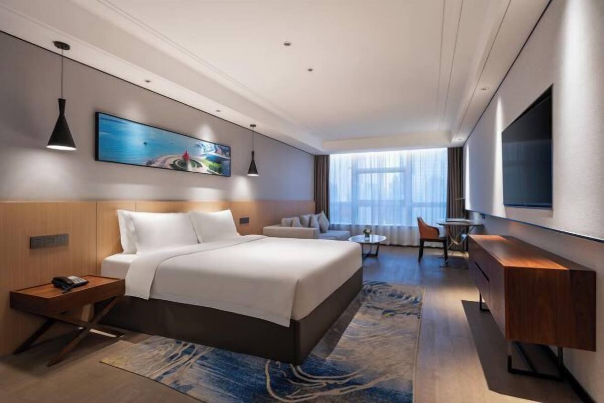 Ein modernes Hotelzimmer mit einem großen Bett, einem Schreibtisch, einem Sessel, einem Fernseher und einem Bild an der Wand.