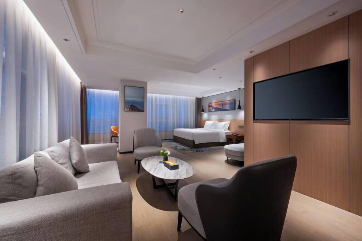 Ein modernes Hotelzimmer mit Sofa, Sessel, rundem Couchtisch und einem Bett.