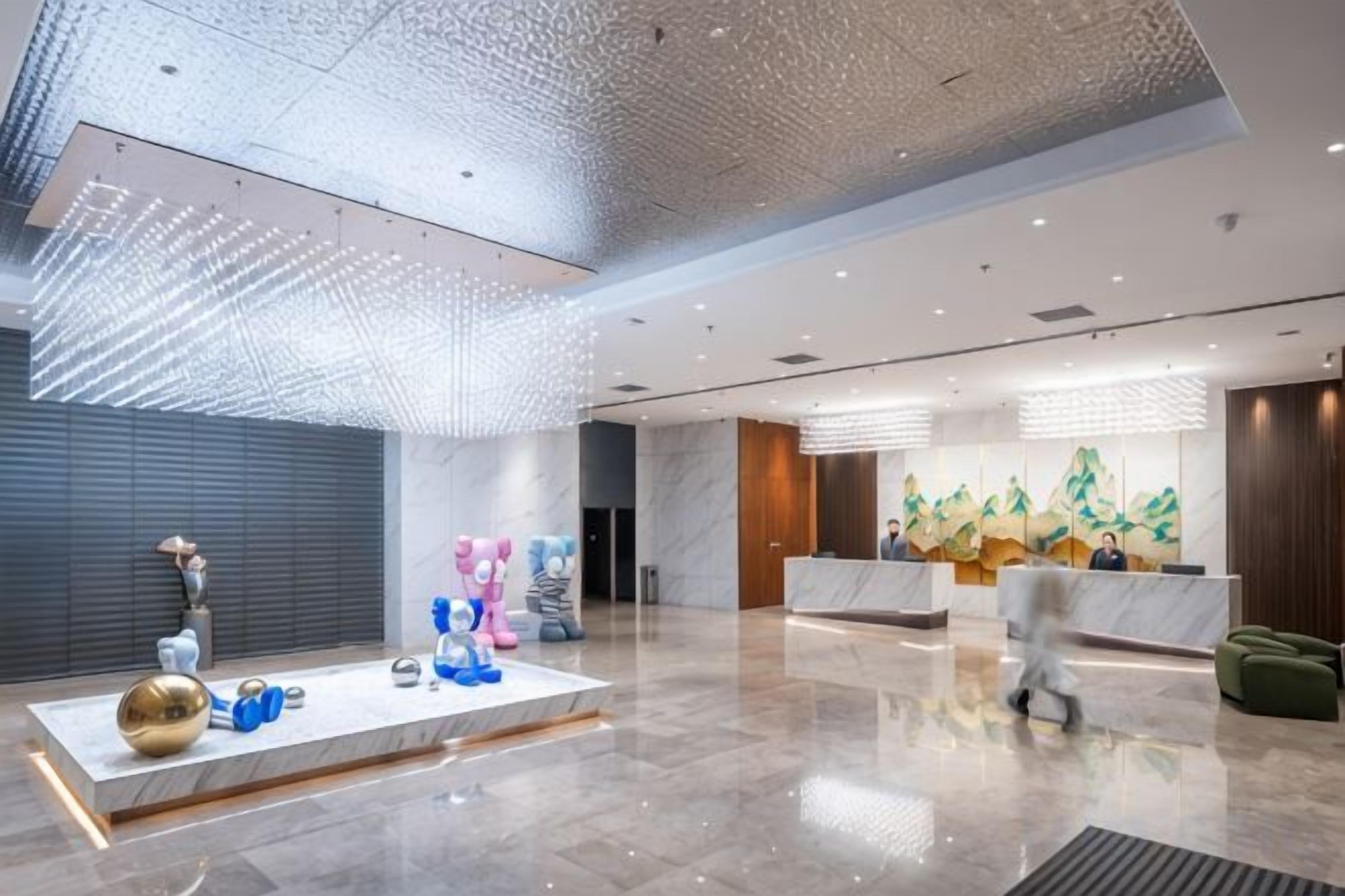 A spacious lobby with a reception desk, a large abstract art piece, and a modern ceiling design.