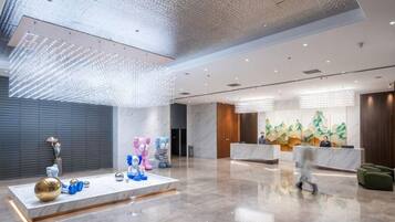 A spacious lobby with a reception desk, a large abstract art piece, and a modern ceiling design.