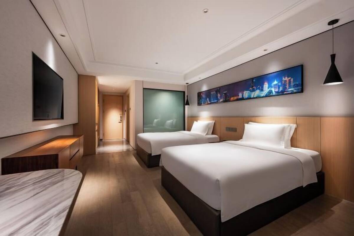 Ein modernes Hotelzimmer mit zwei Betten, einem Fernseher, einem Gemälde und Holzboden.