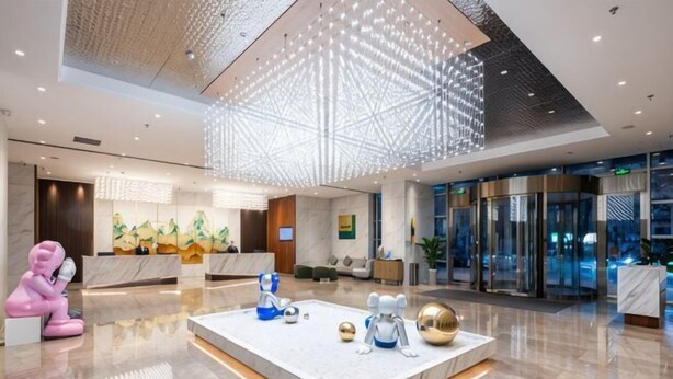 A modern hotel lobby with a reception desk, a large geometric light fixture, and a reception area with a glass door entrance.
