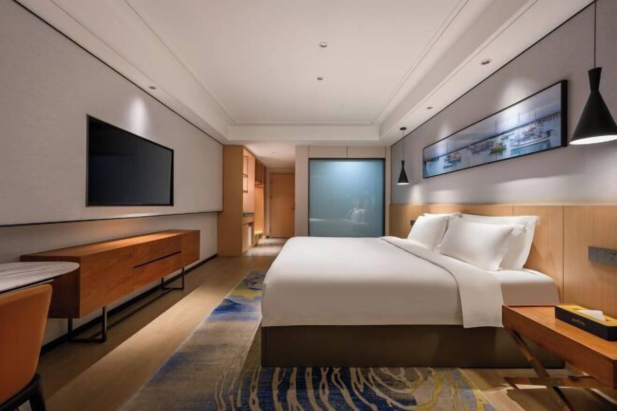 Ein modernes Hotelzimmer mit einem Bett, einem Flachbildfernseher, einem Schreibtisch und einem Nachttisch aus Holz.