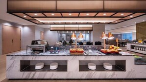 A modern hotel lobby with a marble reception desk, overhead lighting, and a seating area with tables and chairs.