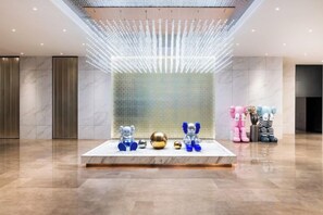 A lobby with a marble floor, a reception desk with a glass partition, and a wall with a textured pattern. - Madison Hotel Qingdao City Center (May Fourth Square) (Qingdao)
