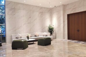 A modern lobby with a marble wall, a sofa, two ottomans, a coffee table, and a wooden door.