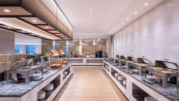 A modern buffet with multiple food stations, marble countertops, and a central walkway.
