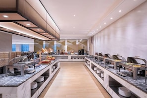 A modern buffet with multiple food stations, marble countertops, and a central walkway. - Madison Hotel Qingdao City Center (May Fourth Square) (Qingdao)