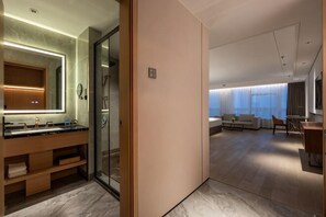 Ein modernes Hotelzimmer mit Bad, einer Sitzecke inklusive Sofa und einem Esstisch, sowie einem großen Fenster.