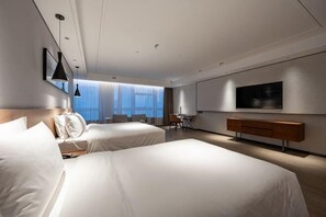 A hotel room with two beds, a desk, a chair, a TV, and a large window.