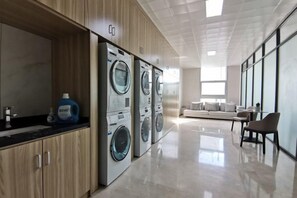 Uma lavanderia moderna com várias máquinas de lavar, uma pia e um janelão que oferece muita luz natural.