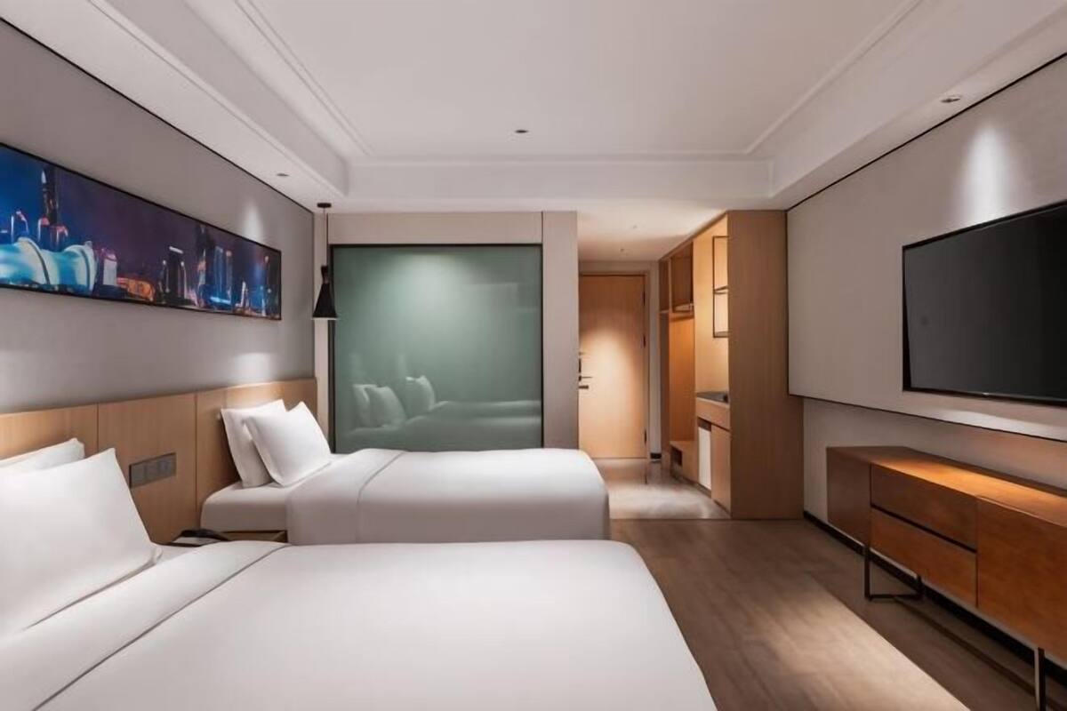 Ein Hotelzimmer mit zwei Betten, einem Flachbildfernseher, einem Bild an der Wand und Blick auf die Stadtlandschaft.