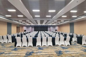 A conference room with rows of white chairs, a stage at the front, and a carpeted floor. - Madison Hotel Qingdao City Center (May Fourth Square) (Qingdao)