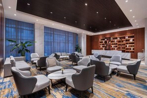 A spacious lounge area with multiple seating options, a marble reception desk, and a large bookshelf. - Madison Hotel Qingdao City Center (May Fourth Square) (Qingdao)