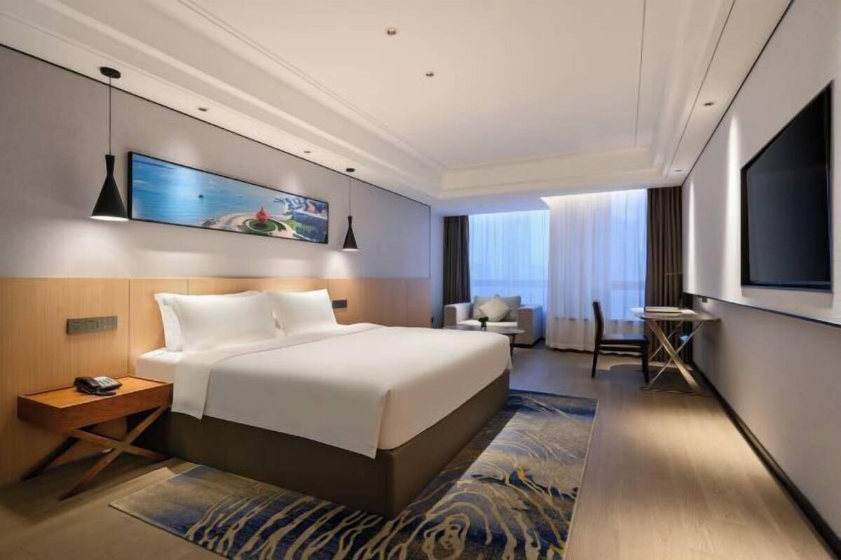 Ein modernes Hotelzimmer mit einem großen Bett, einem Flachbildfernseher, einem Schreibtisch und einem Sessel.