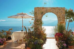 Un área de estar al aire libre con un arco de piedra, una mesa con sombrilla y plantas en macetas.
