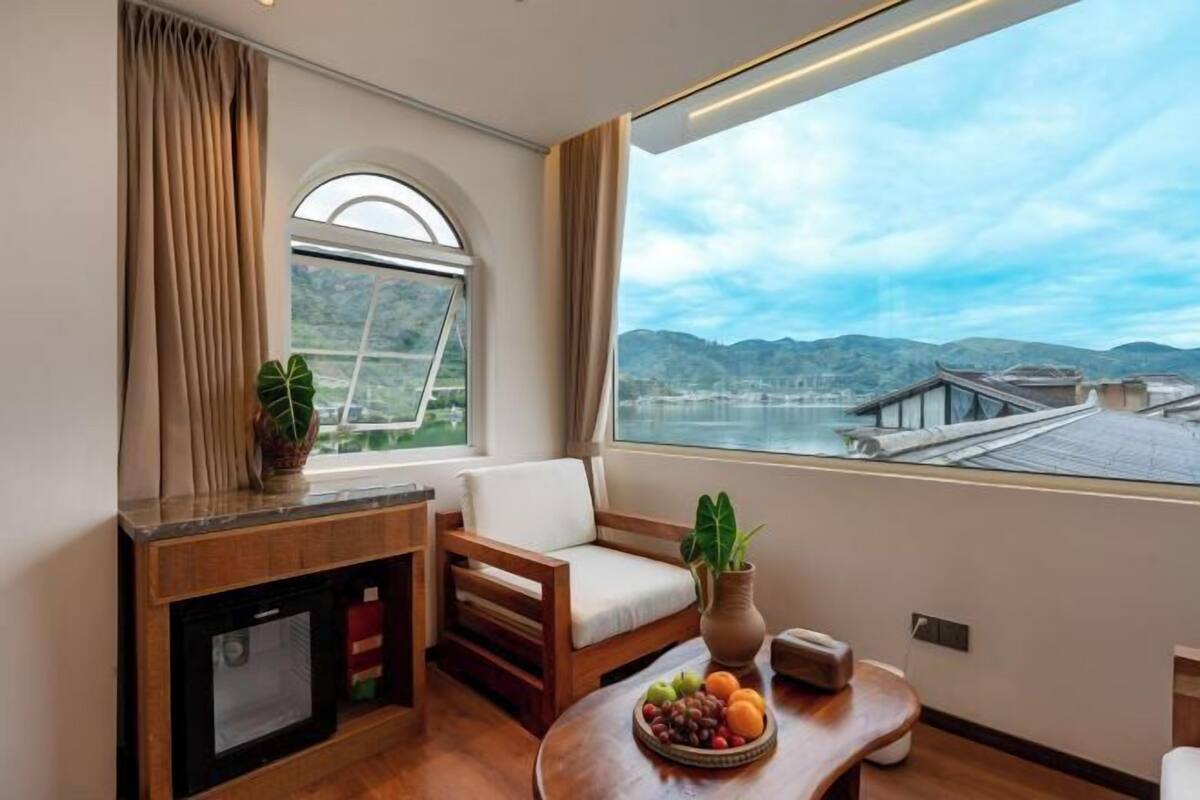A room with a view of mountains, a dining table with fruit, a sofa, and a TV.