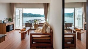 A modern room with a large sliding glass door leading to a balcony with a view of the sea and mountains. There is a wooden bench and a small table with fruits. - Dali Nuan Nuan Ying Jing Cliff Sea View Hotel (Dali City)