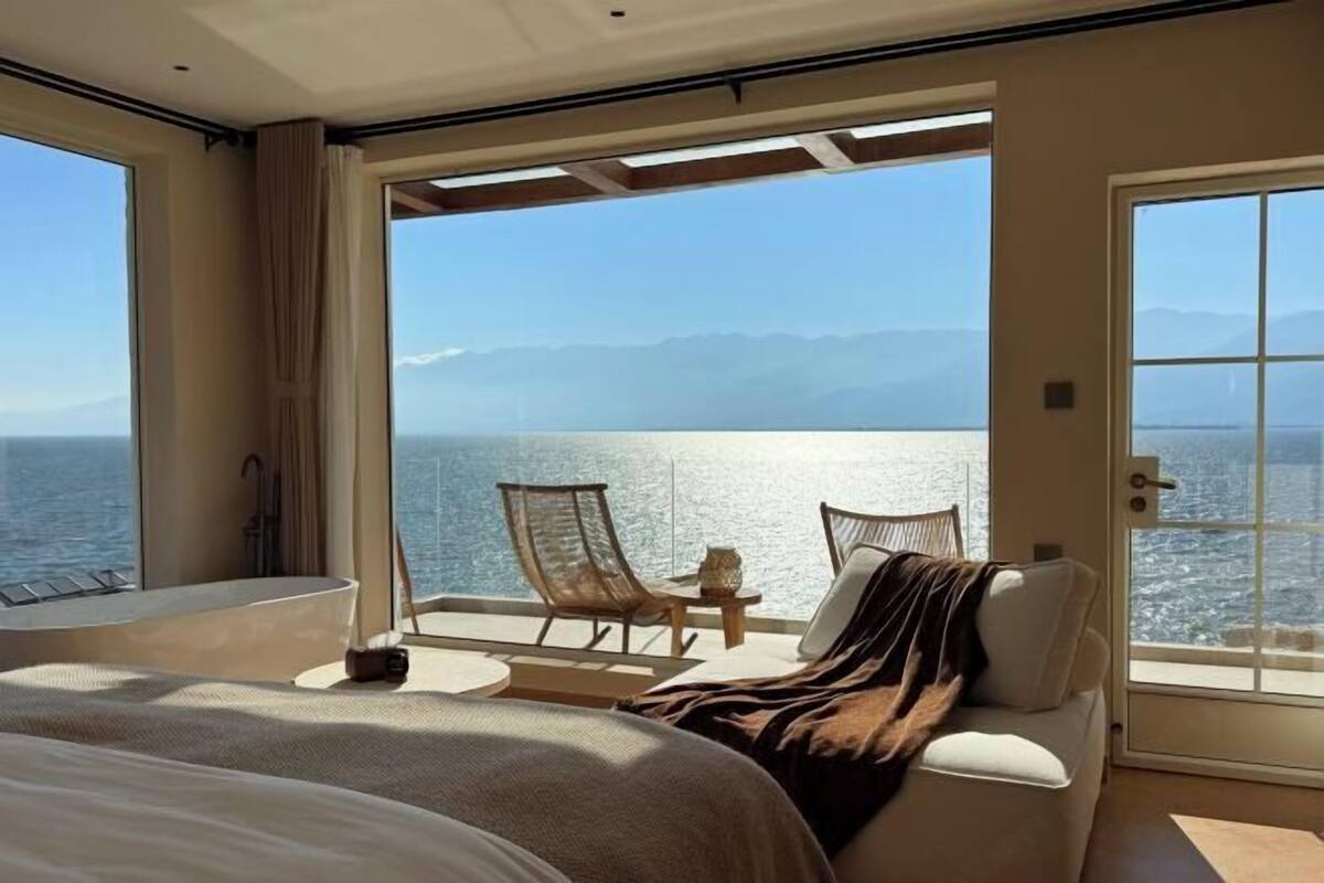 A bedroom with a large bed, a sofa, and a view of the sea.