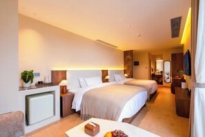 A hotel room with two beds, a small desk with a lamp, a minibar, and a TV.