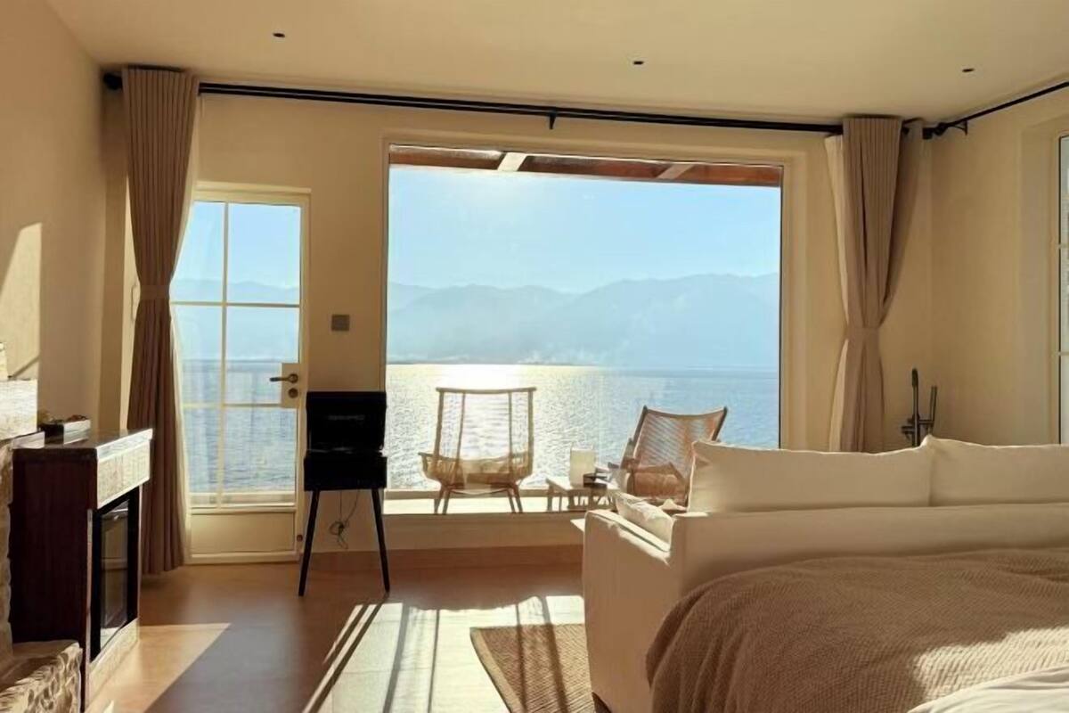 A bedroom with a large window, a bed, a chair, and a desk.