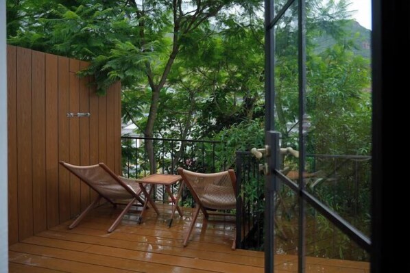 A wooden deck with two wicker chairs and a small table, surrounded by lush greenery.