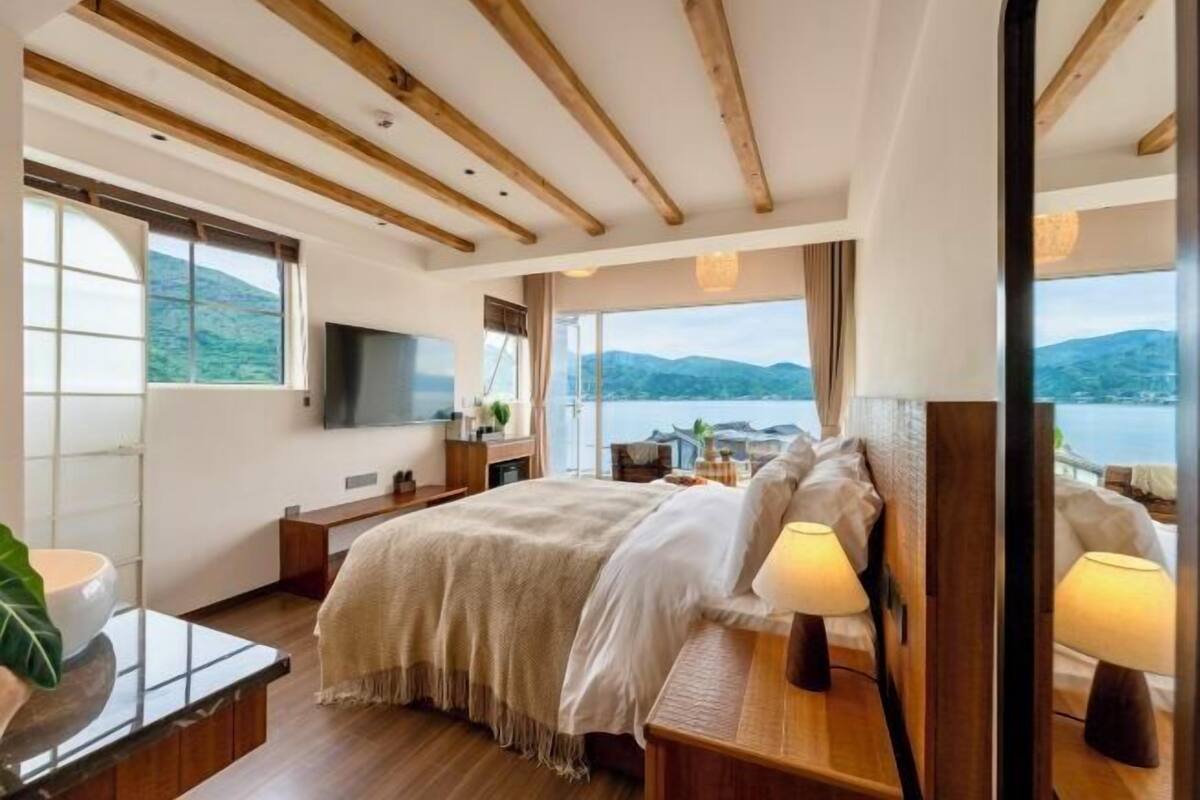 A bedroom with a bed, bedside tables, a TV, and a view of the mountains.