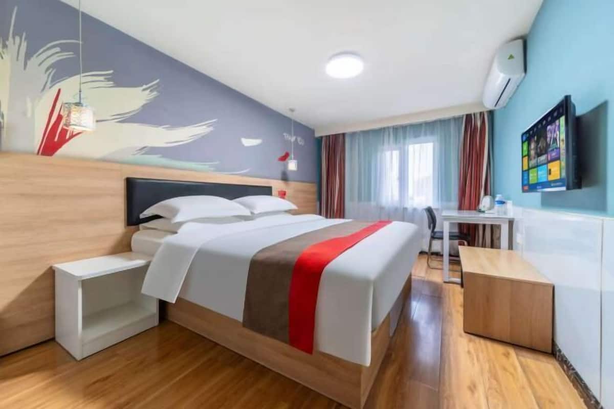 Una habitación de hotel con cama, escritorio, silla y televisor en la pared.
