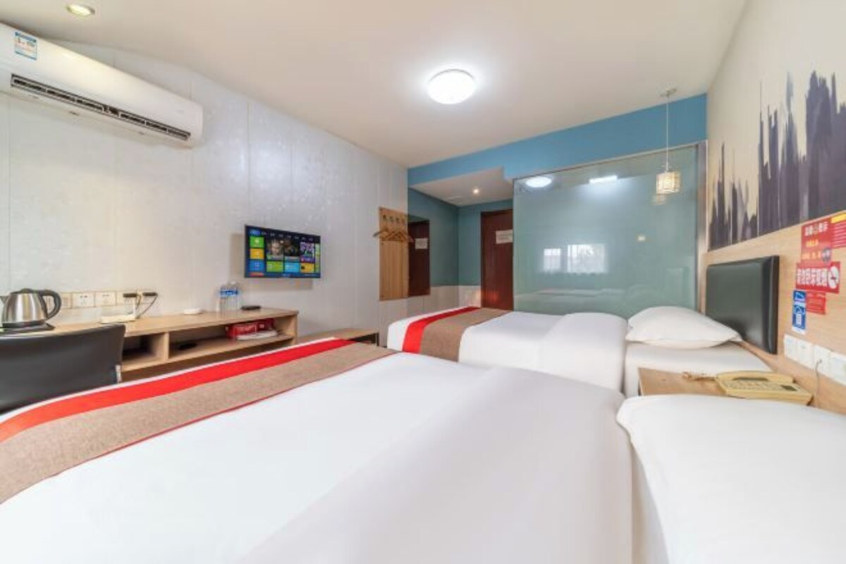 Una habitació d'hotel amb dos llits, un escriptori, una cadira, un televisor i un aire condicionat fixat a la paret.