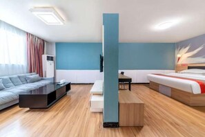 Habitació d'hotel moderna amb un sofà, una taula de cafè, un llit, una televisió i un paviment de fusta.