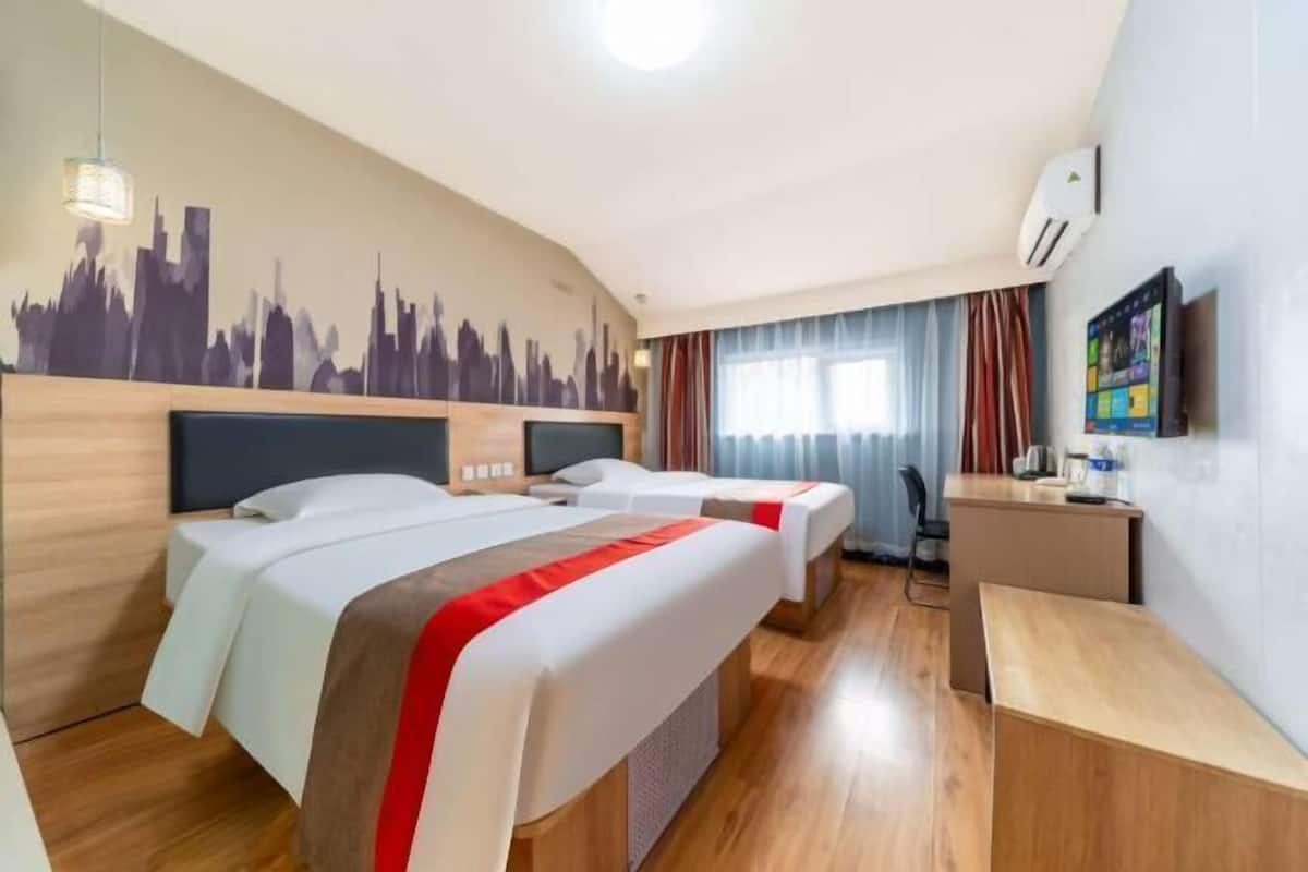 Habitación de hotel con dos camas, un escritorio, una silla, un televisor y un mural con vista a la ciudad en la pared.