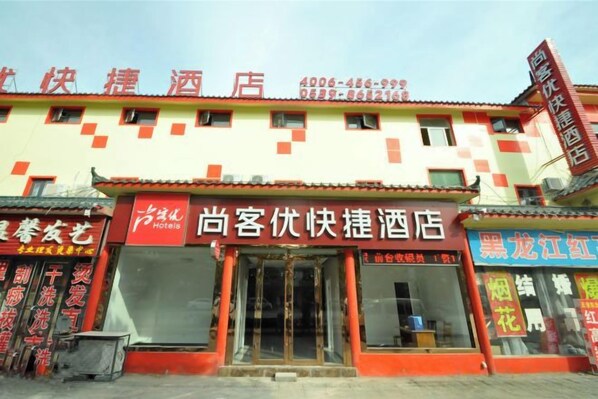 A hotel facade with a red and white color scheme, a visible entrance, and signage indicating the hotel's name and contact information.