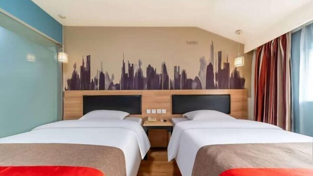 A hotel room with two beds, a cityscape mural on the wall, a wooden headboard, and a nightstand with a lamp. - Shankee Hotel (Linyi Baishabu) (Linyi)