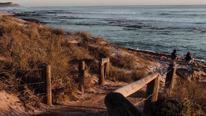 Ein Küstenpfad mit Holzzaun, der zum Strand führt.