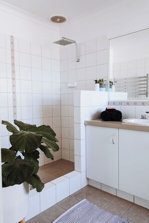 Et moderne badeværelse med hvide fliser, en bruser, en vask og et spejl.