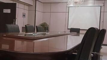 Une salle de conférence avec une longue table, des chaises, un écran de projection et un lustre.